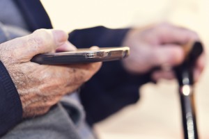 old man with a walking stick uses a smartphone